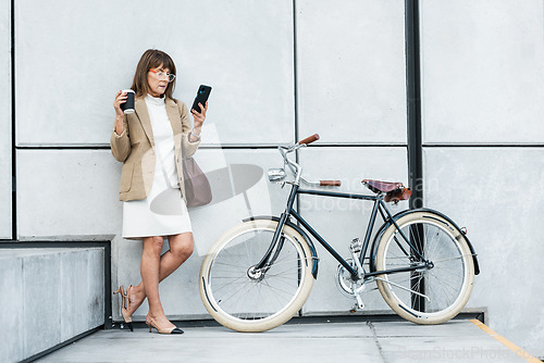 Image of Business woman, phone and coffee with bicycle for eco friendly transport for travel on city break while online with 5g network. Entrepreneur on break using mobile app for communication and networking