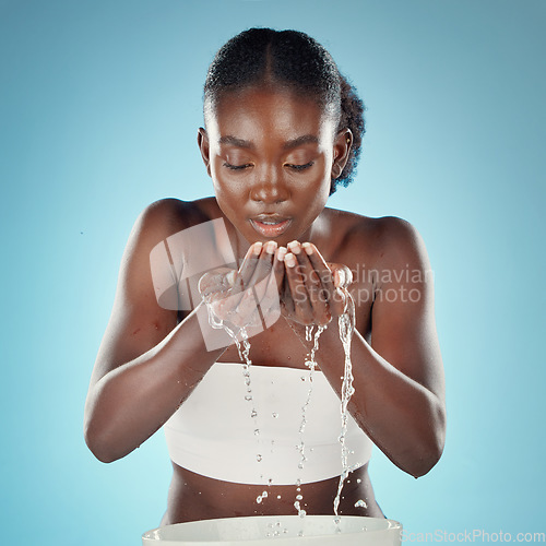 Image of Black woman, water or washing face on blue background in studio for skincare hygiene, healthcare wellness or self care. Beauty model, facial grooming and cleaning splash with hands from sink or basin