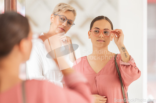 Image of Glasses, buying and mirror check of a woman and shop assistant in a eye clinic or retail store. Lens care, sight test and young customer shopping for frames at an optometrist and shop reflection