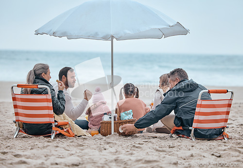 Image of Family, beach food and relax on holiday, vacation or trip outdoors on sandy seashore. Back view, bonding and grandparents and mom, dad and kids enjoying quality time together under beach umbrella.