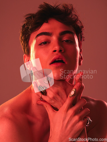 Image of Beauty, cosmetics and man in studio with red lighting to model with jewellery, makeup and designer rings. Creative art, lgbt and portrait of young male pose for skincare, beauty products and fashion