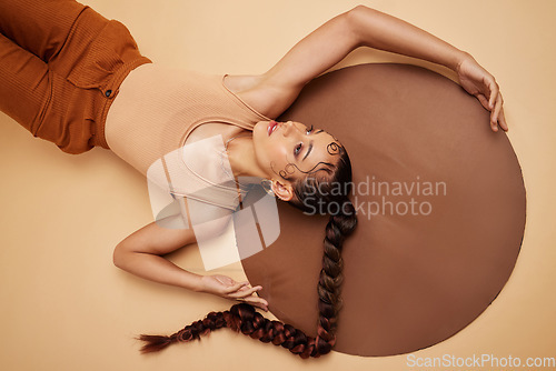 Image of Creative, art and beauty with a model woman lying in studio on a beige background with a circle prop from above. Fashion, design and artistic with an attractive young female on the ground or floor