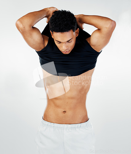 Image of Young man, bodybuilder and taking off shirt for wellness, posing or masculine model with gray studio background. Macho male, confident and muscular with abs, pride for fitness or body care for health