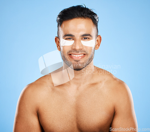 Image of Beauty, skincare and eye patch with grooming and man in wellness for skin portrait against blue studio background. Eye care, healthy face and fresh glow with smile, clean with hygiene and cosmetic.