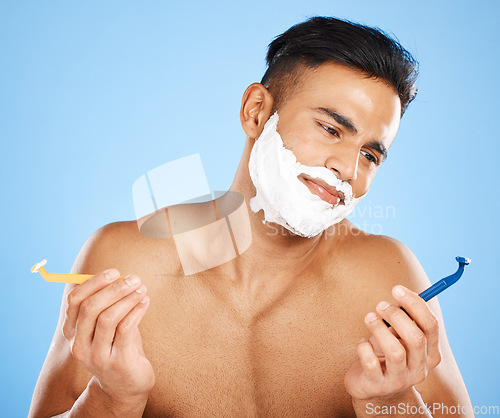 Image of Man, razor and shaving in studio for choice, confused or thinking of skin, cosmetics or performance. Model, shaving cream or blade for shave, grooming or skincare for hair on face by blue background