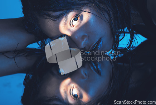 Image of Face, beauty and reflection with a model woman in studio on a blue background against a mirror for skincare. Luxury, art and creative with an attractive young female mirrored in glass for wellness