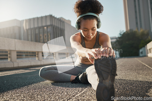 Image of Stretching, foot and city black woman on floor with headphones, sneakers and training gear for outdoor running, exercise and workout. Sports, fitness and girl listening to music for muscle warmup