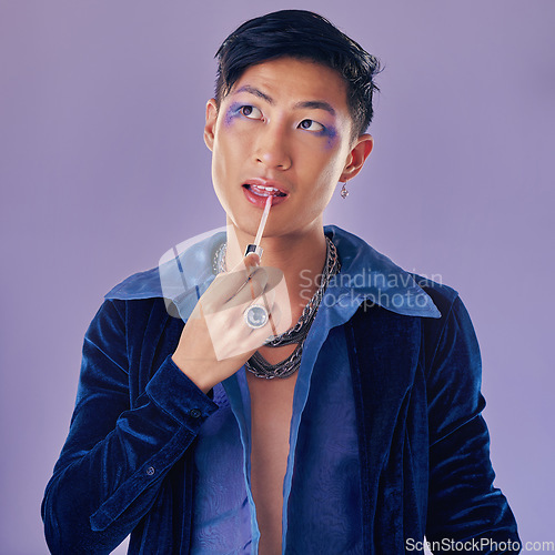 Image of Beauty, makeup and lgbt Asian man in studio on purple background using cosmetics, beauty products and lipstick. Creative, fashion and queer or lgbtq male model with lip gloss, eyeshadow and style