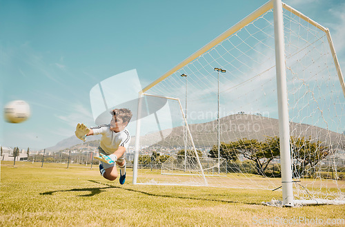 Image of Soccer, sports and children with a goalkeeper saving a shot during a competitive game on a grass pitch or field. Football, kids and goal with a male child diving to save or stop a ball from scoring