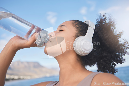 Image of Fitness, headphone and woman drinking water after running, training and cardio workout at beach. Exercise, runner and thirsty with healthy liquid for hydrate, energy and wellness listening to music