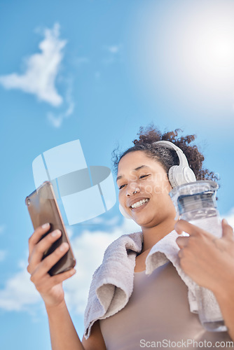 Image of Headphones, phone and woman with water bottle outdoors streaming music, radio or audio. Social media, networking and low angle of female on 5g mobile or text message after training or running workout