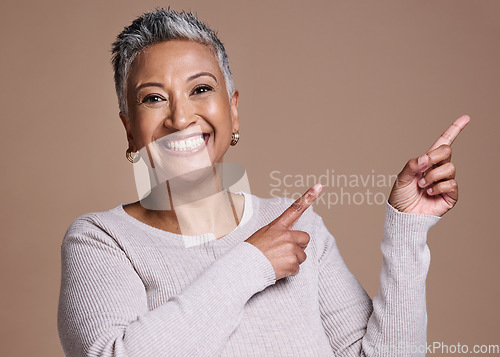 Image of Woman, smile and happiness in studio for advertising free space, promo or mockup on a brown background for cosmetics, makeup or fashion. Face portrait of a mature model pointing finger at mock up