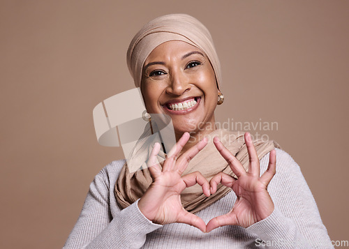 Image of Islam woman, heart and sign with smile, happy and peace against brown studio background. Muslim lady, mature female and hand gesture for happiness, love and commitment for humanity and positive.