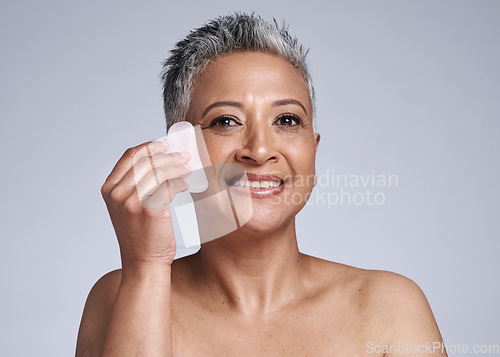 Image of Elderly, woman and portrait of massage with gua sha stone for wellness, circulation and beauty. Skincare model massaging face with natural crystal for facial treatment in gray studio mockup.