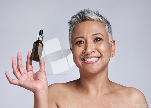 Image of Senior woman, serum and skincare with smile for natural beauty, organic facial and wellness in grey studio background. Body care, model and with cosmetic oil for smooth skin, glow or happy to hydrate