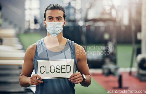 Image of Covid, gym and man holding closed sign during the pandemic while wearing a face mask. Coronavirus, health center and quarantine lockdown with fit, strong male in empty gymnasium