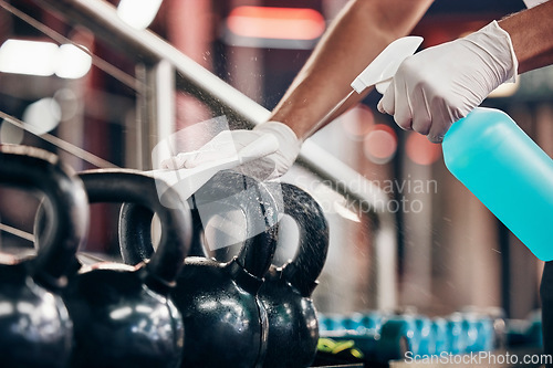 Image of Kettlebell, cleaning service and hands cleaning at a gym with liquid soap in spray bottle with cloth in gloves. Janitor or cleaner wipes dirty bacteria on dusty weights or fitness training equipment