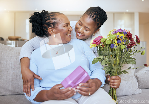 Image of Black woman, mothers day and hug with flowers on sofa for love, box or gift to mom in home. Woman, bouquet and senior mama with wow, smile or happy for surprise, celebration or birthday on couch