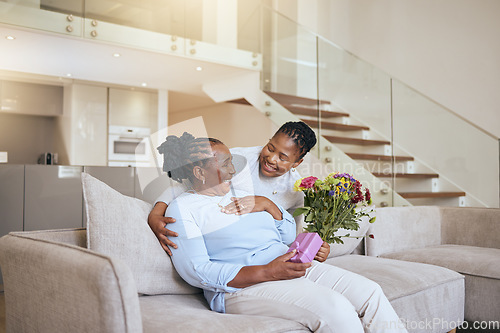 Image of Mothers day, black woman and surprise flowers on sofa for present, box or gift to mom in living room. Woman, bouquet or senior mama on couch with wow, happy or smile for love, celebration or birthday