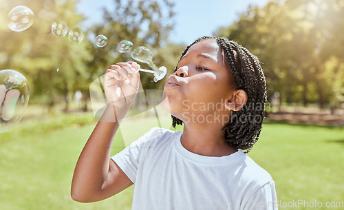 Image of Park, child and black girl blowing bubbles enjoying fun time alone outdoors, joy and childhood development. Happy, freedom and kid learning and playing with soap bubble toy or wand and relax on grass