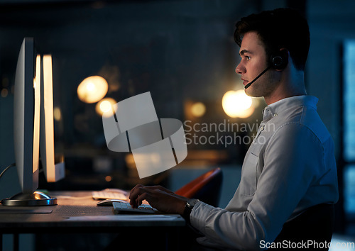 Image of Call center, night office and employee typing, working late shift or overtime for commission. Crm, contact us and telemarketing, sales agent or support worker in dark office consulting on computer.