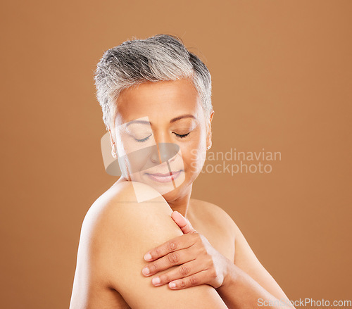 Image of Face, skincare and senior woman with eyes closed in studio on a brown background. Aesthetics, makeup and cosmetics of mature female model from India touching skin or arm for healthy skincare routine.