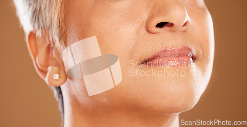 Image of Face, lips and beauty with a mature woman in studio on a brown background to promote cosmetics. Mouth, skincare and wellness with a senior female model posing for natural skin or lip treatment