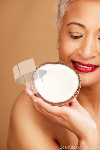 Image of Beauty, skincare and coconut with a senior woman in studio on a brown background to promote natural antiaging care. Cosmetics, moisture and hydration with a mature female posing with a fruit half