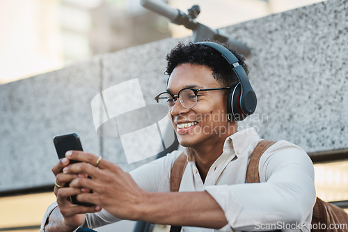 Image of Music, phone and city with a business black man streaming or listening to music while networking. Schedule, mobile and street with a male employee using headphones to stream audio in an urban town