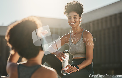 Image of Fitness, headphones and black women or friends in city on break with water bottle and talking. Health, wellness and people resting while streaming music, radio or podcast after running or training.