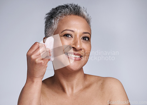 Image of Portrait, happy and senior woman gua sha, face and smile in grey studio background. Elderly woman, skincare model and wellness care of healthy skin with facial treatment with beauty cosmetic tool