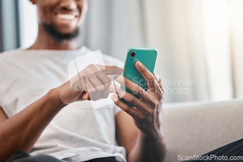 Image of Hands, phone and social media with a black man typing a text message while sitting on a sofa in his home. Mobile, communication and networking with a male chatting from the living room in his house