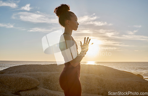 Image of Yoga, meditation or sunset with woman in peace by the ocean, sea or beach for wellness, zen or chakra balance. Spiritual, health or fitness girl on rock or sand for mindset goal, pilates or workout