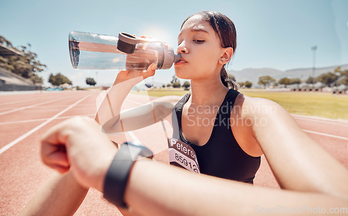 Image of Drinking water, time and running with a sports woman checking her watch during a workout on track. Fitness, exercise and hydration with a female athlete tracking her progress during cardio training