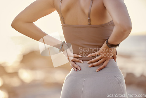 Image of Back pain, fitness and beach woman workout with training, exercise and spine muscle injury. Tired athlete by the ocean sea with healthcare, medical and joint sprain accident or problem in nature