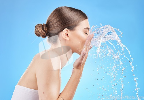 Image of Skincare, water and woman cleaning face in studio on blue background for wellness, hygiene and facial cleanse. Beauty, hydration and girl washing skincare products, cosmetics and makeup with splash