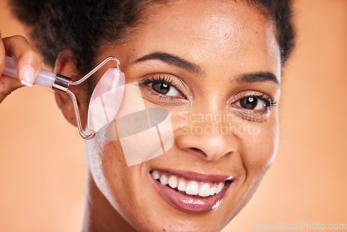 Image of Massage, smile and black woman with a jade roller for facial health, wellness and beauty against orange studio background. Spa, skincare and face portrait of a model with a product for healthy skin