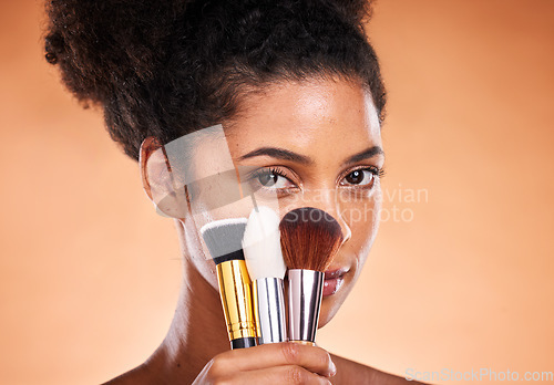 Image of Makeup, brushes and portrait of a black woman in a studio doing a beautiful, natural and cosmetic routine. Cosmetics, beauty and young female model with facial products isolated by orange background.