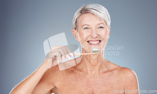 Image of Teeth, dental care and mature woman brushing teeth with toothbrush and toothpaste on gray background with smile on face. Morning routine, healthcare and fresh, happy senior lady in studio portrait.