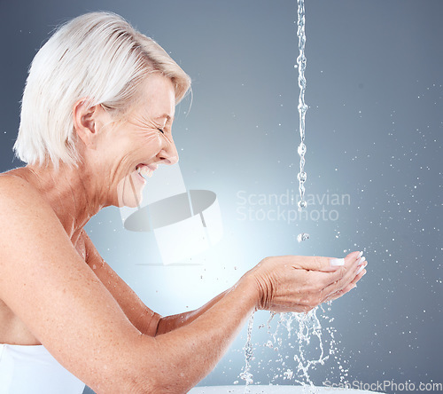 Image of Skincare, happy and senior woman with water for face, beauty and hydration against a grey studio background. Cleaning, wellness and elderly model with a smile for hygiene and grooming with liquid