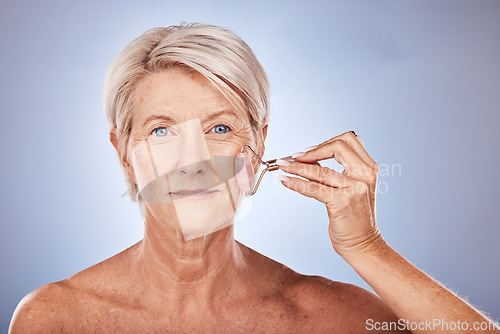 Image of Facial beauty, senior woman with roller for wellness, aesthetic or health makeup, glowing skincare or cosmetics on blue spa studio background. Face product, model or luxury skin portrait for massage