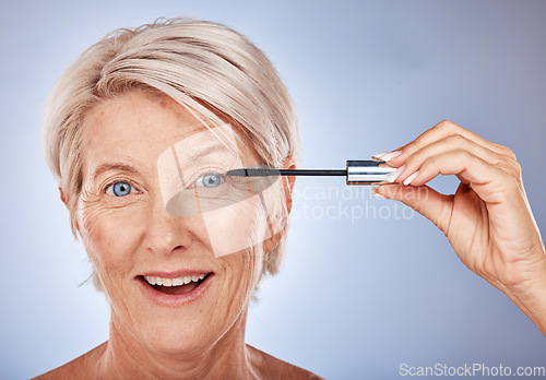 Image of Portrait of senior woman with mascara brush, cosmetic beauty product and makeup wand for eye lashes in Sydney. Surprised smile in studio with gray background, natural blue eyes and luxury skincare