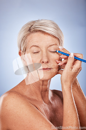 Image of Eyeliner, makeup and senior woman with beauty against a grey studio background. Cosmetic, color and elderly model with focus while applying cosmetics to face and eyelid with pencil during retirement