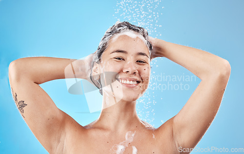 Image of Hair care, smile and Asian woman in the shower for grooming, hygiene and morning routine against a blue studio background. Wellness, happy and beauty model washing hair with foam from shampoo