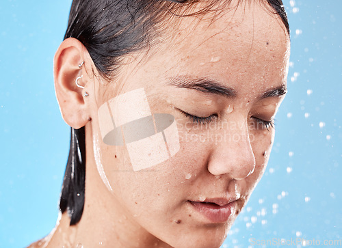 Image of Calm, water and woman in the shower for grooming, hygiene and relax against a blue studio background. Cleaning, skincare and Asian model relaxing during body care for wellness, beauty and routine