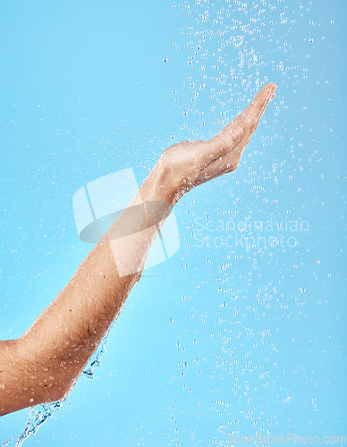 Image of Hand, shower and water for skincare hygiene, wash or dermatology against a blue studio background. Arm and hands of person in healthy wellness, skin hydration and washing for body care treatment