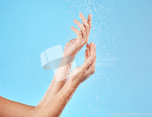 Image of Hand, water and cleansing for health, wellness and bodycare on a blue studio background. Hands, fingers and shower cleaning of body and arms for cleansing, hygiene and grooming flow