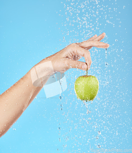 Image of Water, splash and hand with apple in studio for health, nutrition and wellness. Natural diet, healthy eating and person holding fruit with water splash, drop and stream isolated on blue background
