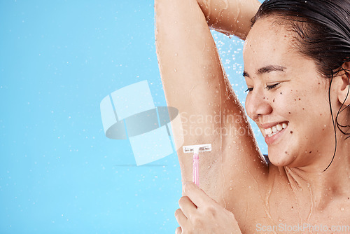 Image of Shower, underarm and shaving with a model asian woman shaving her armpit in studio on a blue background for grooming. Water, luxury and hair removal with an attractive young female in the bathroom