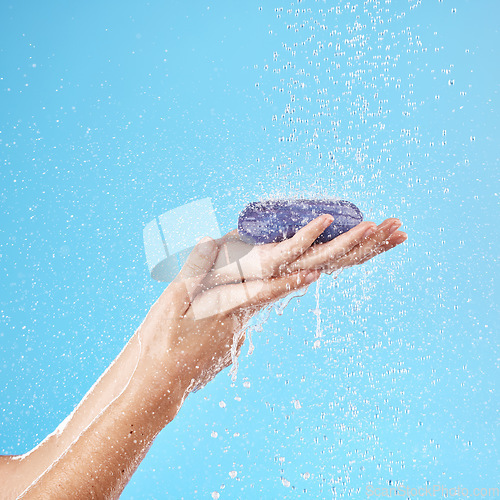 Image of Shower, soap and woman hands in a studio to wash her hands or body for hygiene, wellness or health. Water, clean and closeup of model holding soap bar for self care while isolated by blue background.